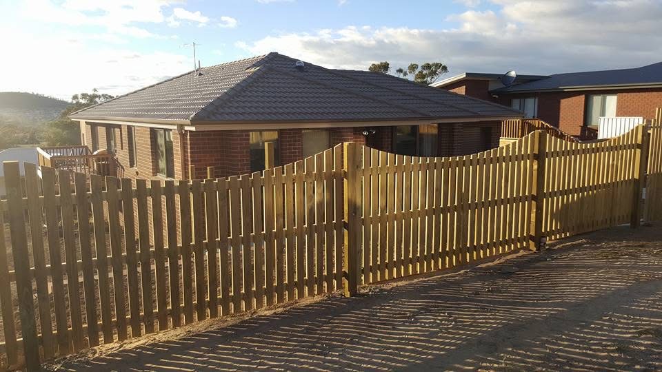 Timber picket fence and double gates in front of a brick home