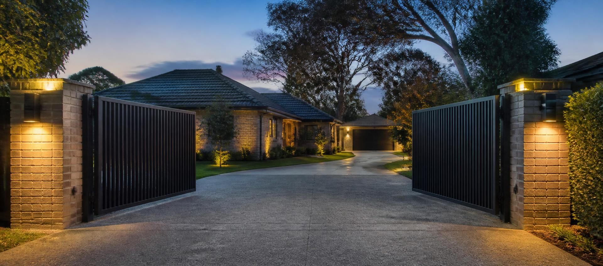 Automatic driveway gates lit at dusk with lighting on the piers