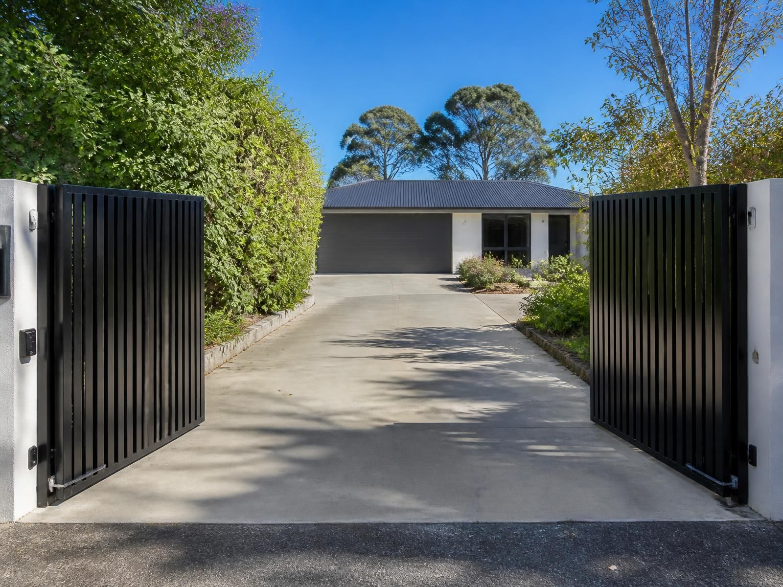 Automated vertical slat double gates open onto a residential driveway