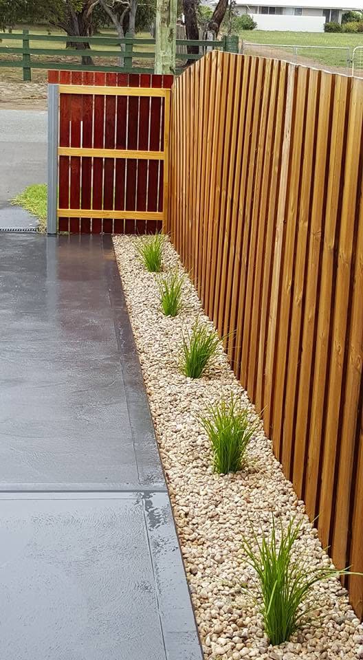 Stained timber swing gate and vertical slat fence beside a concrete driveway